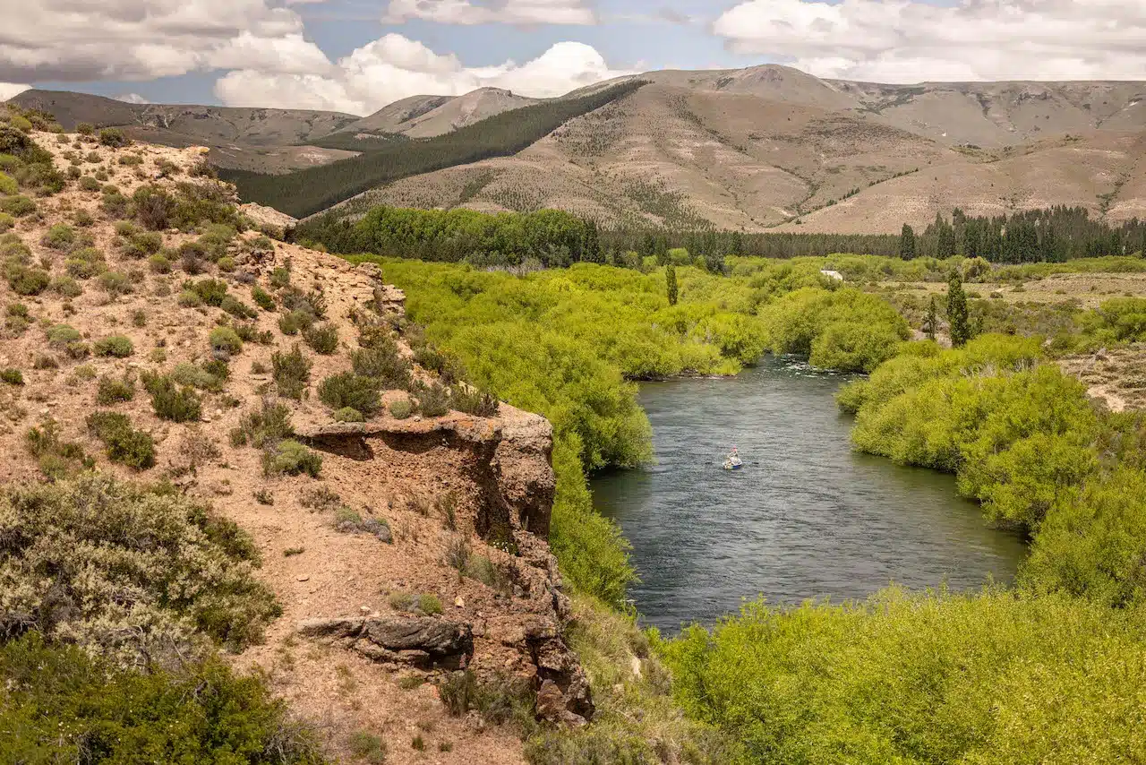 An aerial view of a fishing boat floating down the Chimehuin River in Patagonia between cliffs and trees