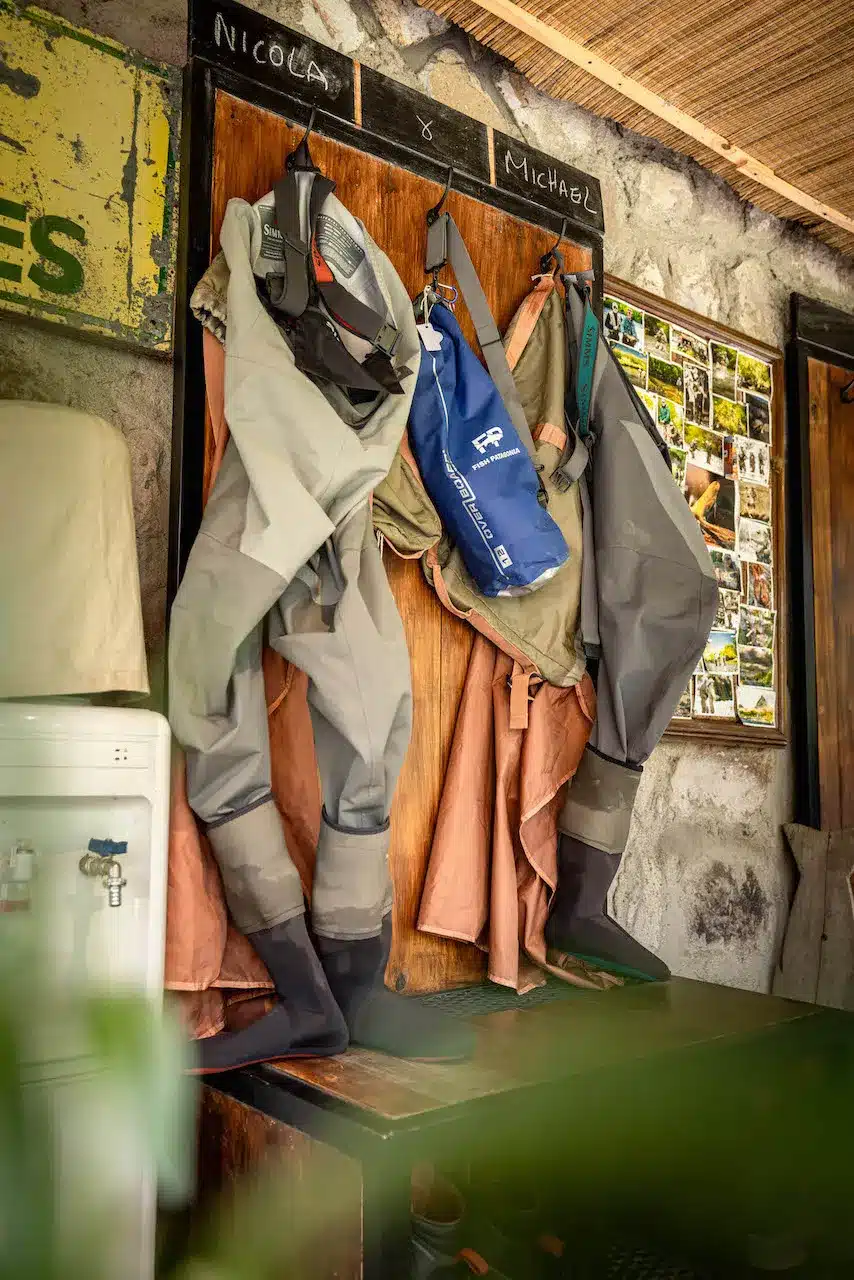 Two sets of waders and dry bags for fly fishing hang from hooks in the outdoor wading room at Tipiliuke lodge in Patagonia