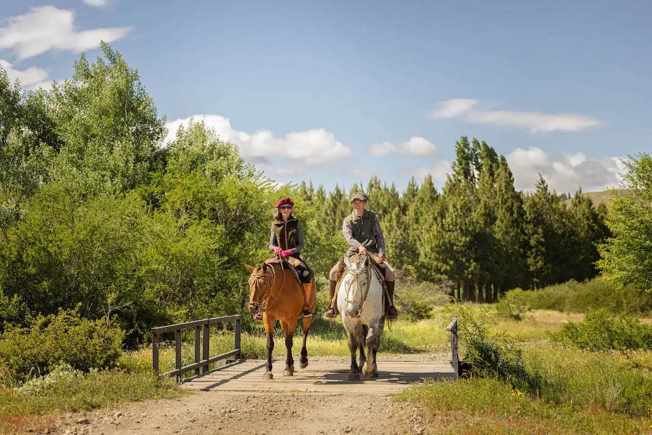 Two riders on horseback crossing a bridge at Tipiliuke Lodge in Patagonia