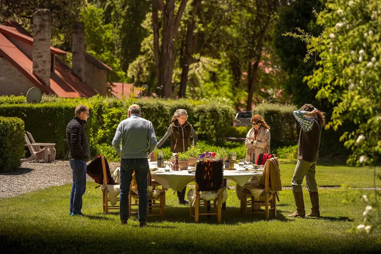 Guests around an outdoor table set for lunch in the gardens at Tipiliuke Lodge in Patagonia