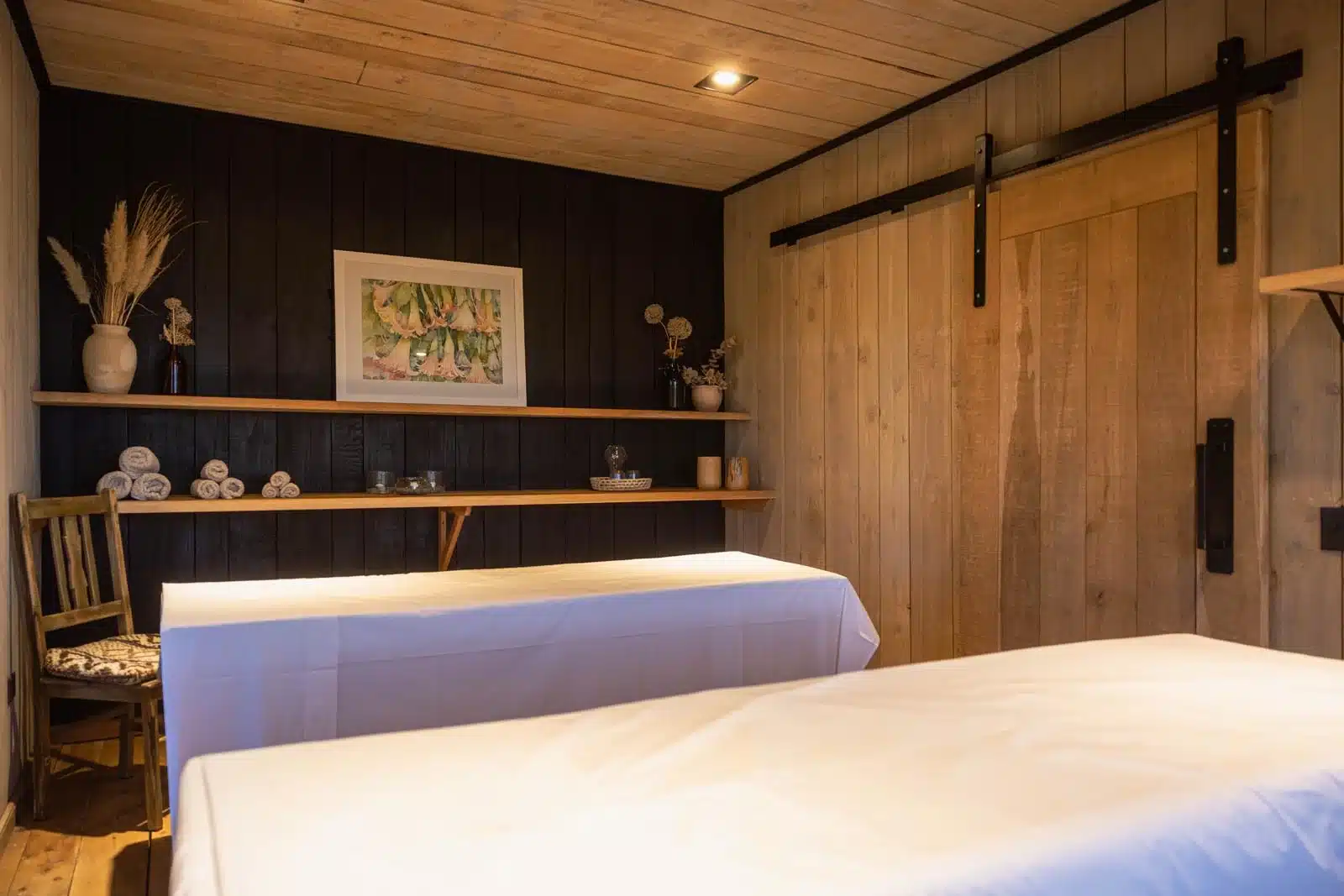 Massage room with two massage beds, decorational shelves and wooden walls at River House Lodge Patagonia