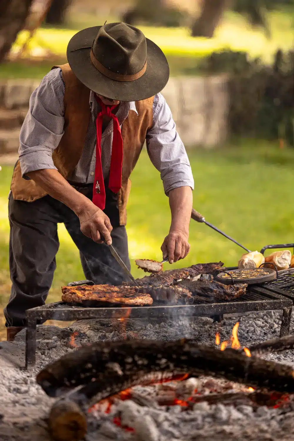 a gaucho bends over an asado serving meat cuts with a large knife