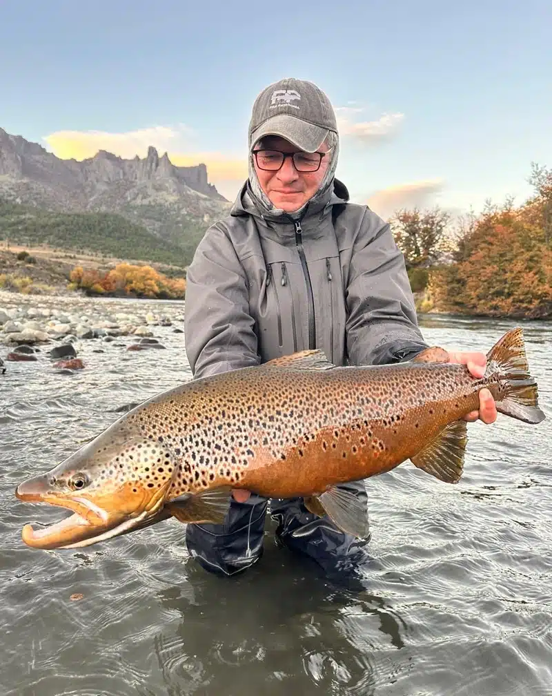 a fisherman holds a huge migratory brown trout out of the water on the Traful River Patagonia