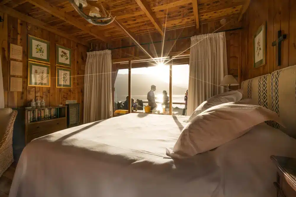 bedroom at the cabin at Arroyo Verde with a double bed and people outside the window overlooking Traful lake